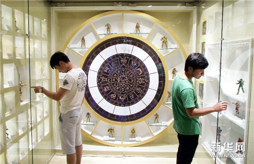 两名男子在南京德基广场观看展出的“黄金圣斗士”人物玩偶