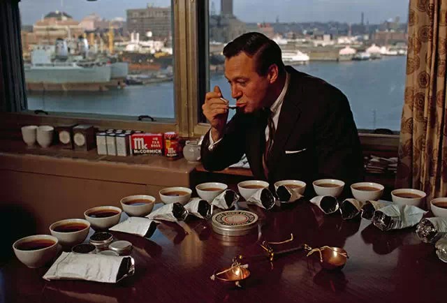 1964年9月，马里兰州，一位职业品茶者正在从桌上的不同茶碗中取样品尝，窗外是一片海港